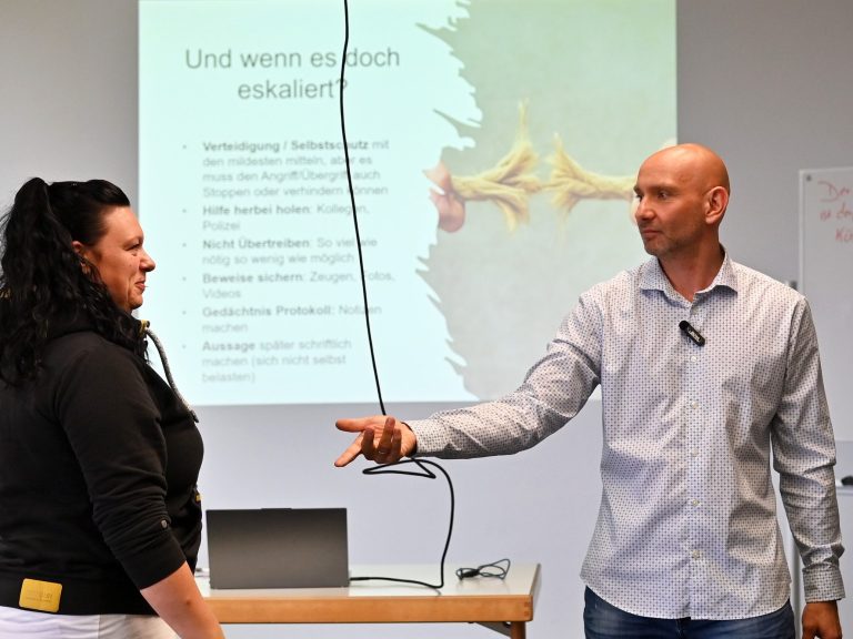 Eine Gruppe von Personen sitzt in einem Raum auf Stühlen, alle schauen aufmerksam nach vorne.