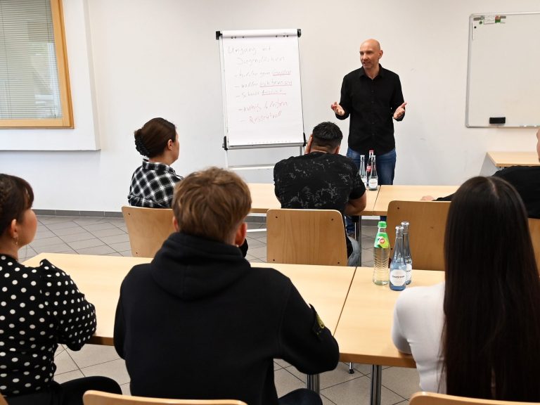 Ein Dozent spricht vor einer Gruppe von Teilnehmern in einem Besprechungsraum.